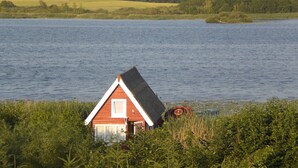 A red house with a sloped roof partially submerged in water, surrounded by greenery. - Bootshaus Direkt am See mit Eigenem Steg an der Ostsee (Sternberg)