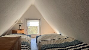 A bedroom with two beds, a nightstand, a lamp, and a window. - Bootshaus Direkt am See mit Eigenem Steg an der Ostsee (Sternberg)