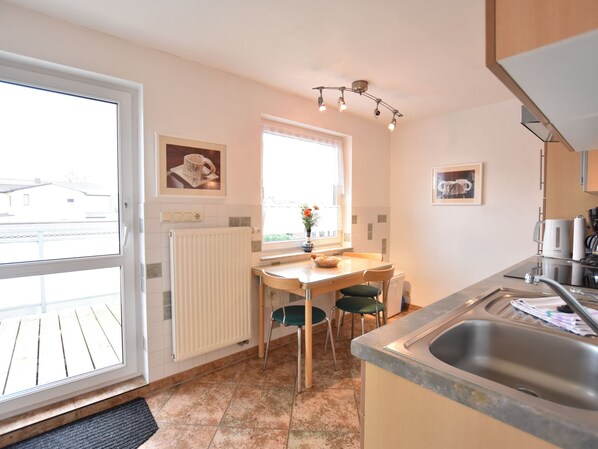 A kitchen with a dining table, chairs, a radiator, a window with a view, and a sink. - Schone Wohnung mit Balkon Nahe Ostseestrand in Rerik (Rerik)