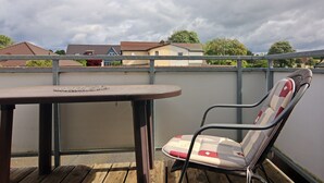 Un balcone con tavolo e sedia, una ringhiera e case sullo sfondo.