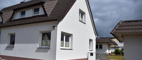 A modern two-story house with a sloped roof, multiple windows, and a small front porch.