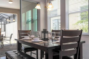 A dining area with a glass table set for four, surrounded by dark wooden chairs. - Solara Resort 4BD Pool Home, Perfect Location 1554 (Kissimmee)