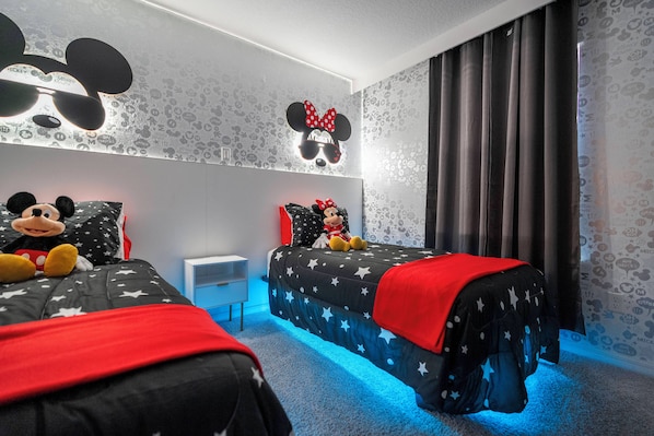 Ein Schlafzimmer mit zwei Betten, beide mit Bettwäsche im Mickey Mouse und Minnie Mouse Design.