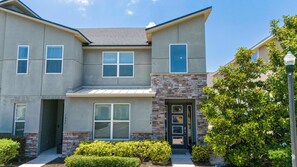 A two-story residential building with a stone facade, large windows, and a well-maintained front yard. - Solara Resort 4BD Pool Home, Perfect Location 1554 (Kissimmee)