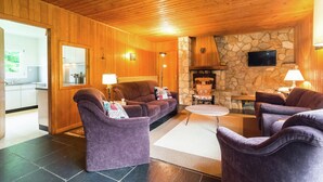 Un salon chaleureux avec une cheminée en pierre, un plafond en bois et des meubles violets.