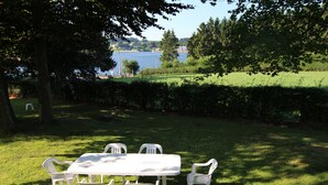 Une table et des chaises blanches sont disposées sur une pelouse verdoyante, avec en arrière-plan un lac et des arbres.