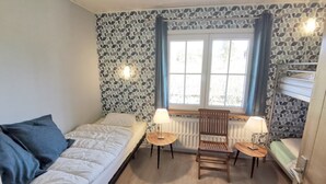 Une petite pièce comprenant un lit, une petite table avec une chaise, un radiateur et une fenêtre avec des rideaux.