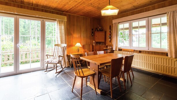 Un espace repas avec une table et des chaises en bois, de grandes fenêtres et un ventilateur de plafond.