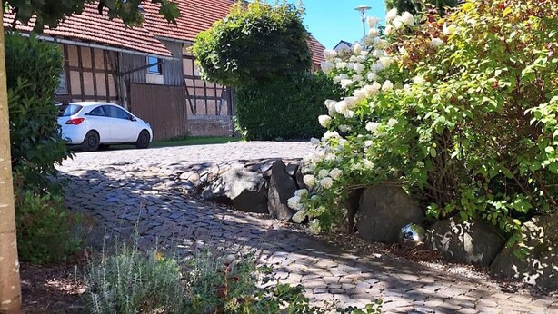 Een straatje van cobblestones leidt naar een witte auto, geparkeerd voor een huis met een rode dakbedekking.