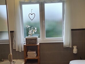 A bathroom with a window, a wicker basket, and a shelf with folded towels.