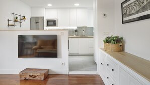 A modern kitchen with white cabinets, a stainless steel refrigerator, and a microwave. There is a wooden floor and a large painting on the wall. - Always Easy I San Martin (San Sebastián/Donostia)