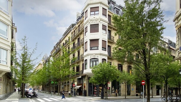 A street view with a building featuring a corner entrance, a pedestrian crossing, and trees lining the sidewalk. - Always Easy I San Martin (San Sebastián/Donostia)
