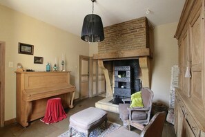 A room with a fireplace, wooden furniture, a piano, and a hanging light fixture. - Unique Holiday Home in Virton with Hot Tub (Habay)