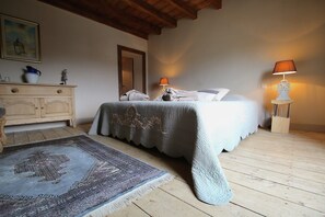Um quarto com uma cama, duas luminárias de cabeceira, um aparador de madeira, um tapete e um quadro na parede.