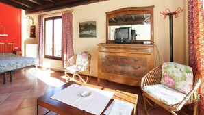 A cozy room with a wooden ceiling, a bed, a dresser, two wicker chairs, and a television on the dresser.