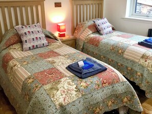 A bedroom with two beds, each with floral-patterned bedding and matching pillows. A red lamp is on the nightstand between the beds. - Tidereach - Otters View - UK12269 (Connel, near Oban)