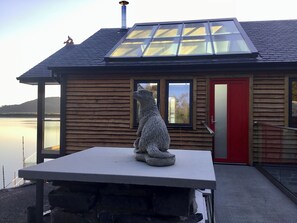 A wooden cabin with a skylight, a red door, and a stone sculpture on a table. - Tidereach - Otters View - UK12269 (Connel, near Oban)