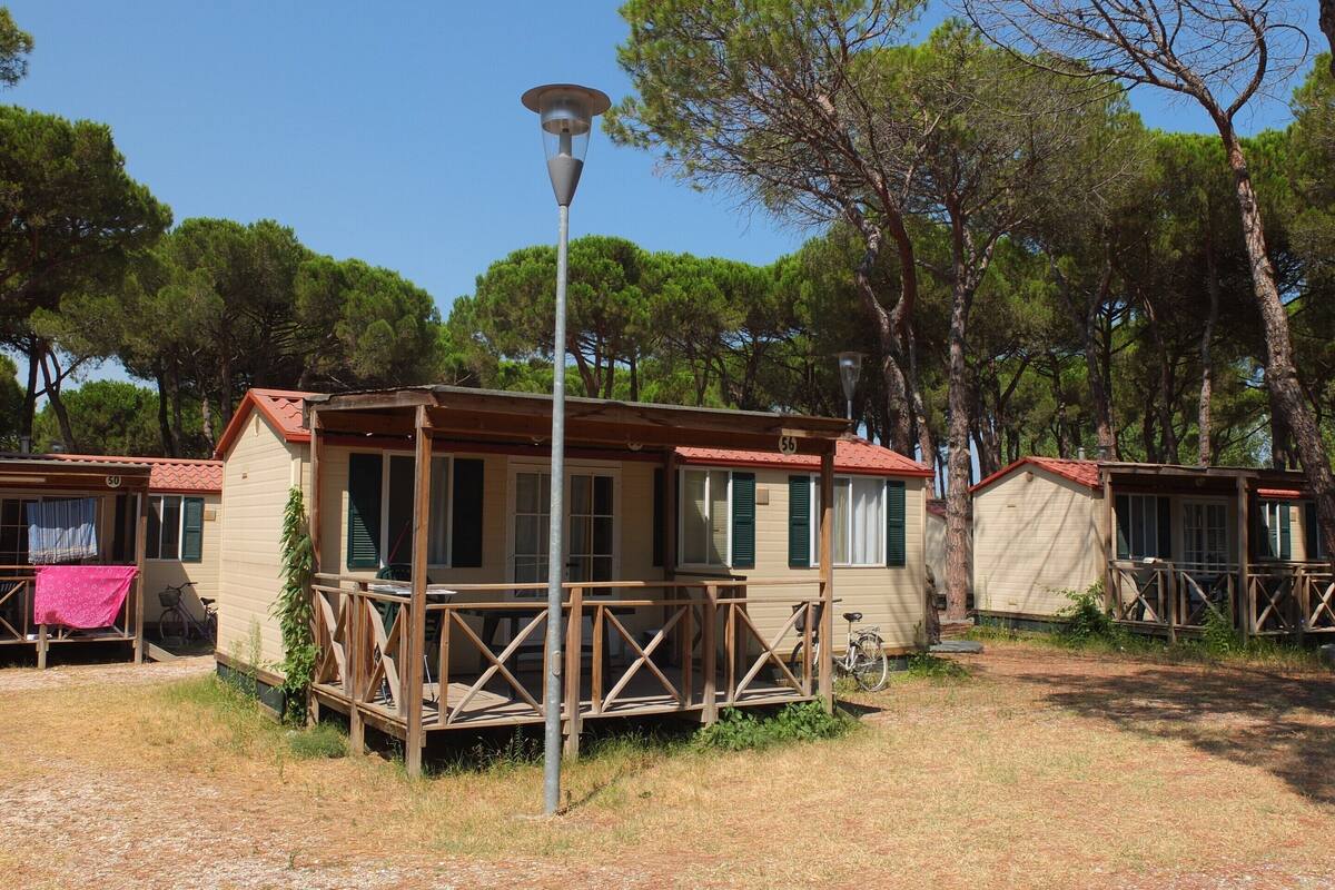 A row of wooden cabins with a metal railing, a street lamp, and trees in the background.