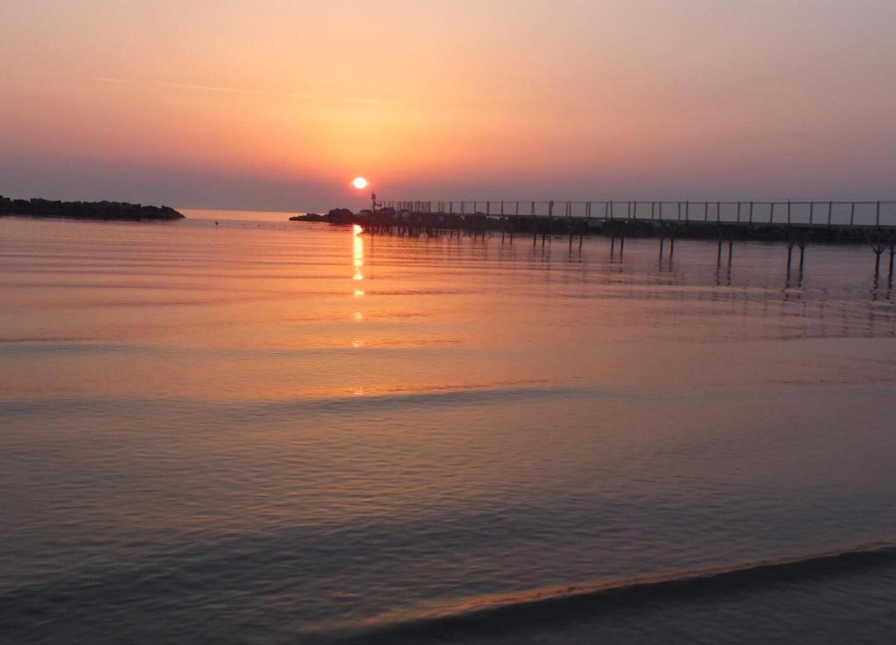 Een zonsondergang boven kalm water, met een steiger die zich in de verte uitstrekt.
