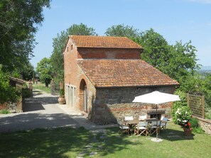 A rustic brick building with a tiled roof, a stone wall, and a small outdoor seating area with a table and chairs. - Cozy Holiday House With Terrace (Castiglion Fiorentino)