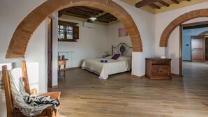 Quarto com cama, assoalho de madeira, arcos de tijolo e um armário de madeira.