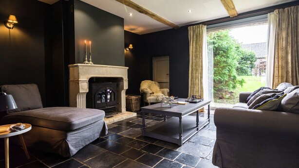 A modern living room with a fireplace, dark walls, and a view of greenery outside. - Cottage in Haut-bois With Private Pool (Gesves)