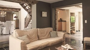 A spacious living area with a beige sofa, a staircase, and a kitchen in the background. - Cottage in Haut-bois With Private Pool (Gesves)
