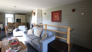 Een woonkamer met een grijze bank, een houten salontafel en een eethoek met rieten stoelen.
