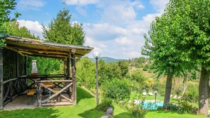A rustic wooden structure with a thatched roof, a stone wall, and a clear view of a swimming pool and lush greenery in the background. - Holiday Home Monte With Pool and Forest Trails (Monte Santa Maria Tiberina)