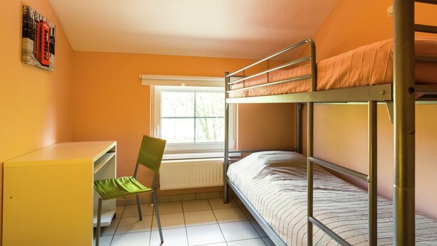 A dormitory room with bunk beds, a desk, a chair, and a radiator.