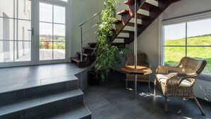 A modern interior with a staircase, a wicker chair, and a view of greenery outside.