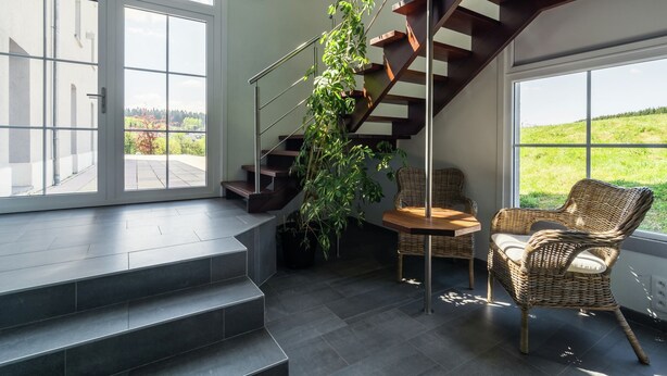 Interior moderno com escada, uma cadeira de vime e vista para o verde lá fora.