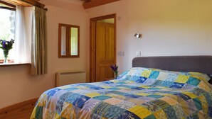 A bedroom with a wooden ceiling, a bed with a colorful quilt, a window with curtains, and a door. - Round House - UK12083 (St Endellion, near Port Isaac)