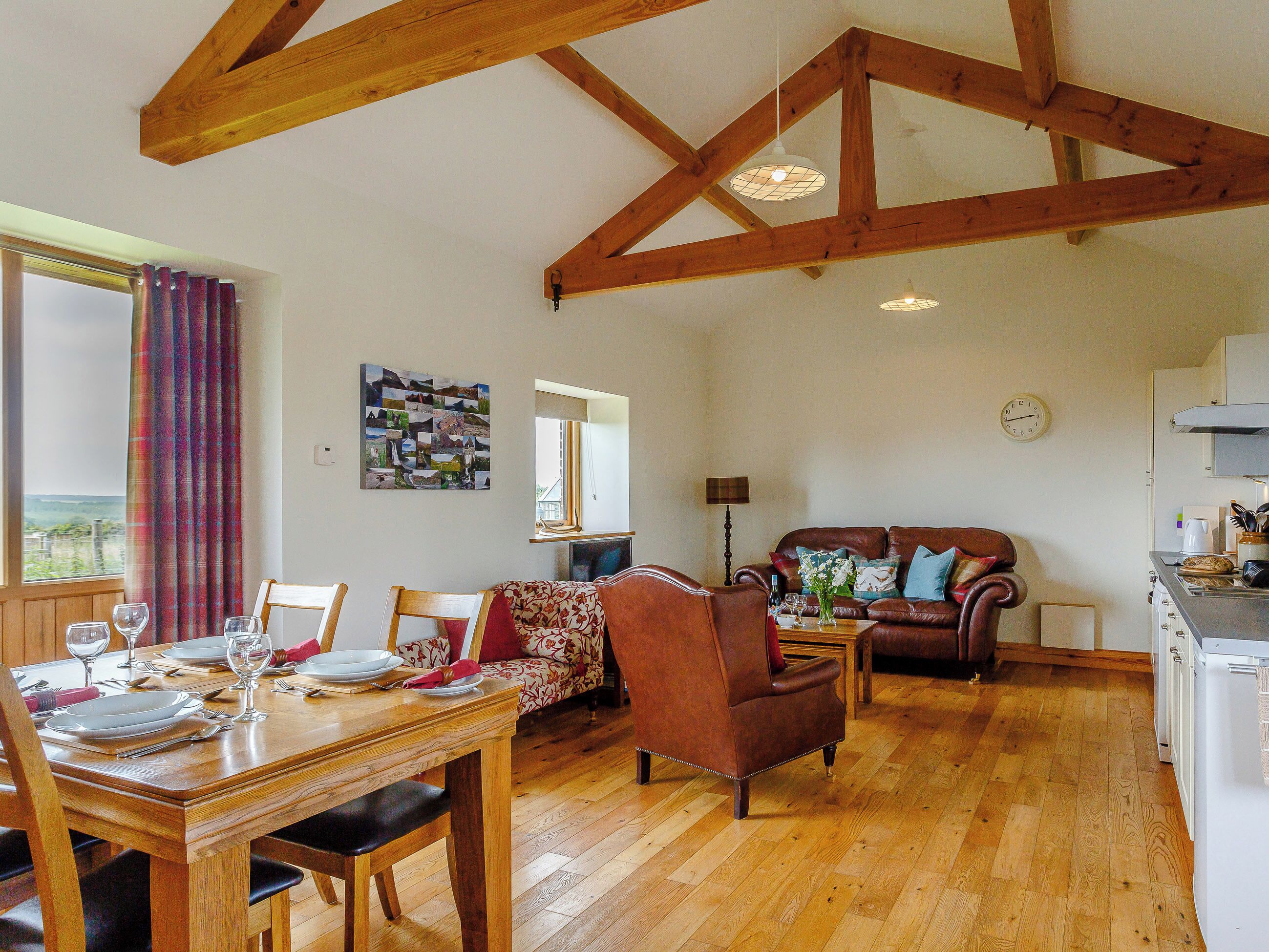 A spacious living area with a wooden dining table set for a meal, a leather sofa, and a kitchen in the background.