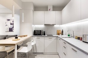 Une cuisine moderne avec des meubles blancs, un four à micro-ondes encastré, une cuisinière à gaz et un évier. On y trouve également un coin repas avec une table et des chaises.