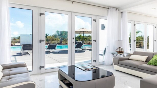 Amplia sala de estar con un sofá grande, una mesa de centro y vistas a una piscina y zona de estar exterior a través de puertas de vidrio.