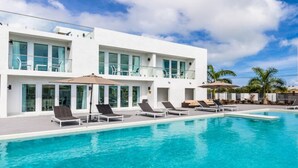 Un hotel moderno con una piscina grande, tumbonas y un cielo azul despejado.
