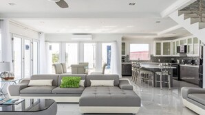 Una sala de estar moderna con un sofá, un reposapiés y una mesa de centro. Cuenta con una zona de cocina con una barra y taburetes.