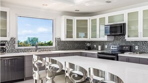 Una cocina moderna con armarios blancos, una isla grande con taburetes de bar, un microondas integrado y un refrigerador de acero inoxidable.