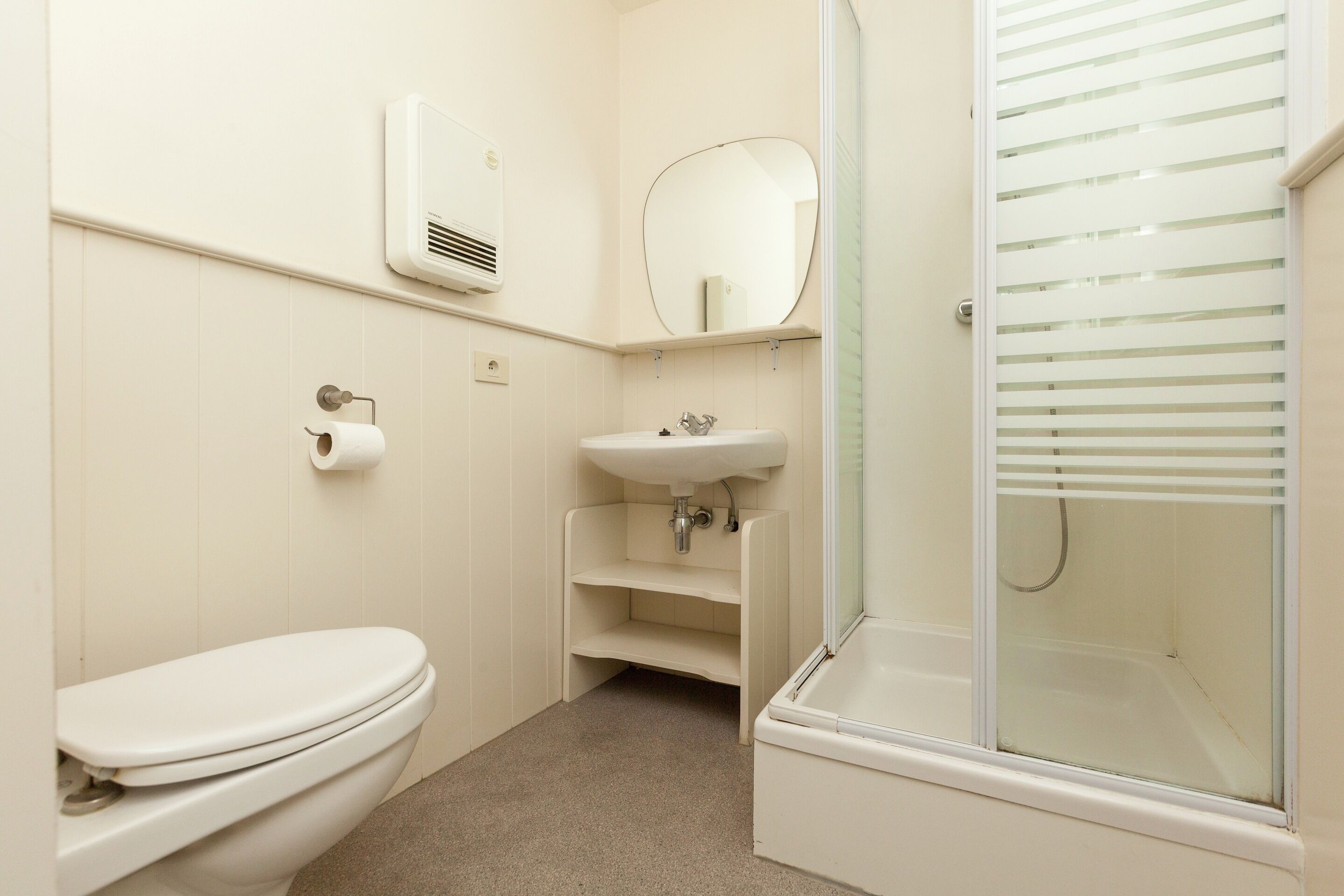 A bathroom with a toilet, sink, mirror, and shower.