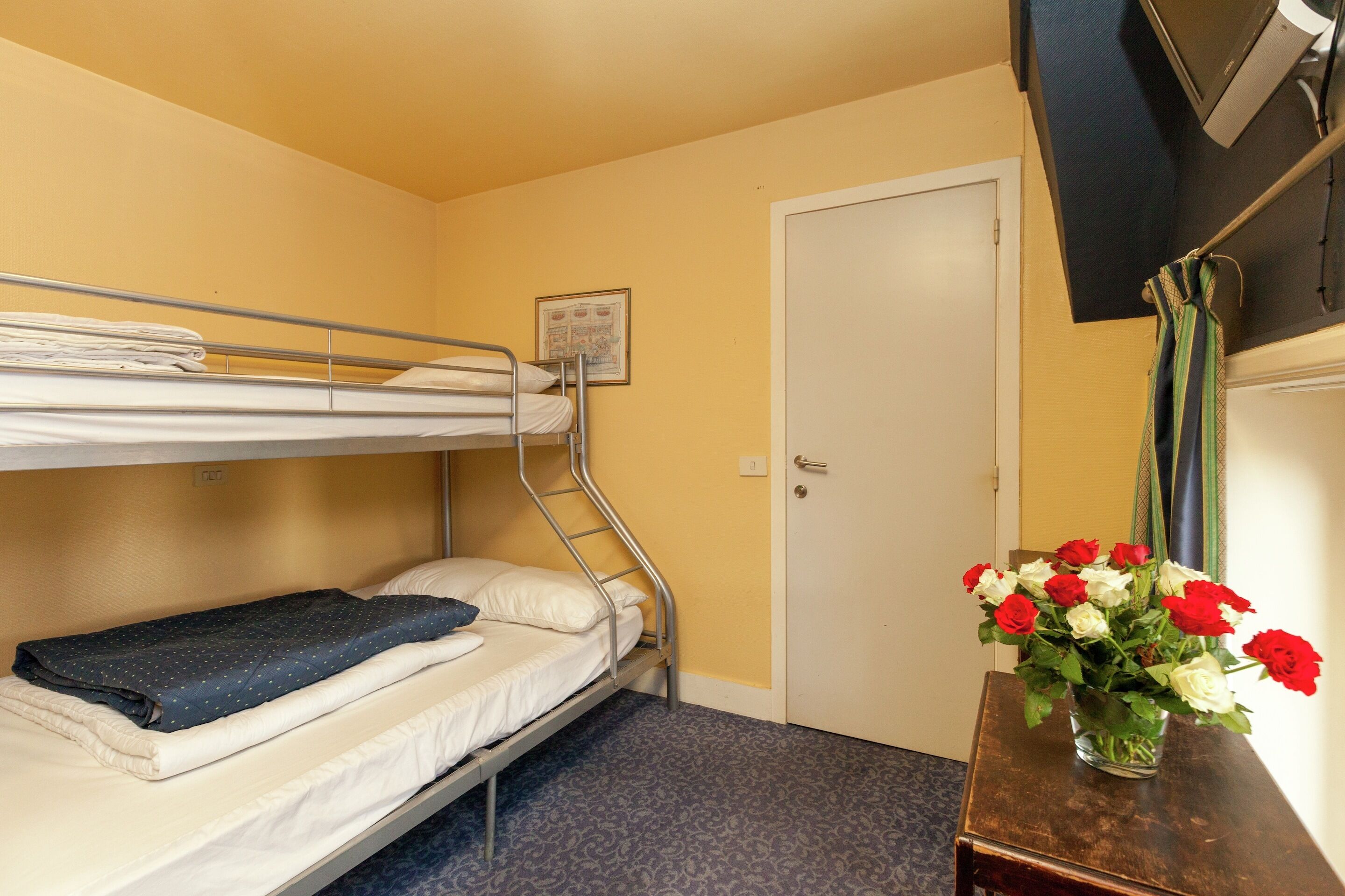 A bunk bed room with a door, a small table with a vase of flowers, and a poster on the wall.