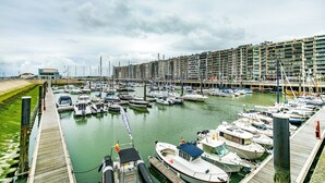 A marina with numerous boats docked, a wooden pier, and a large building in the background.