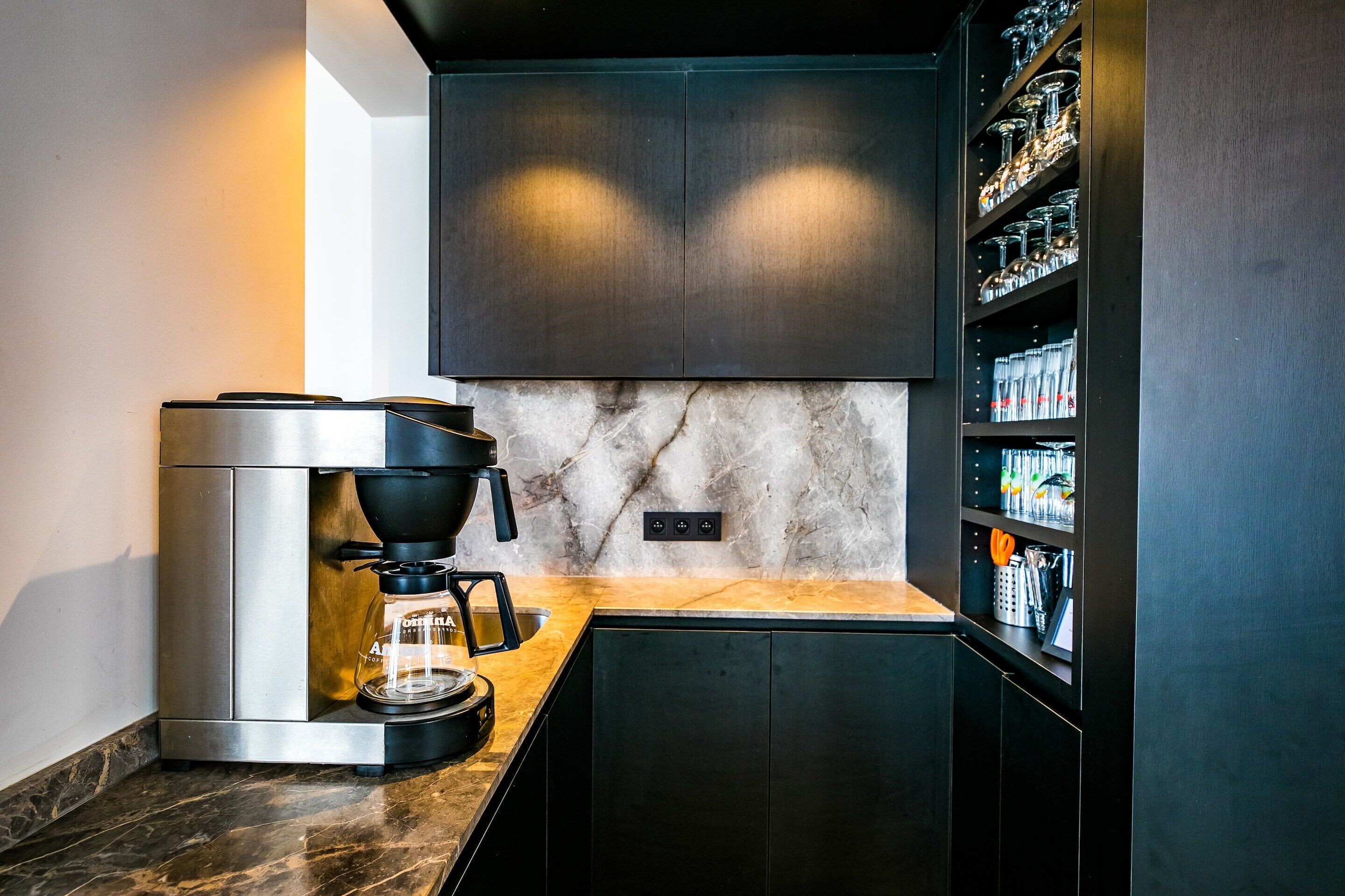 A modern kitchen with a built-in coffee maker, marble backsplash, and dark cabinetry.