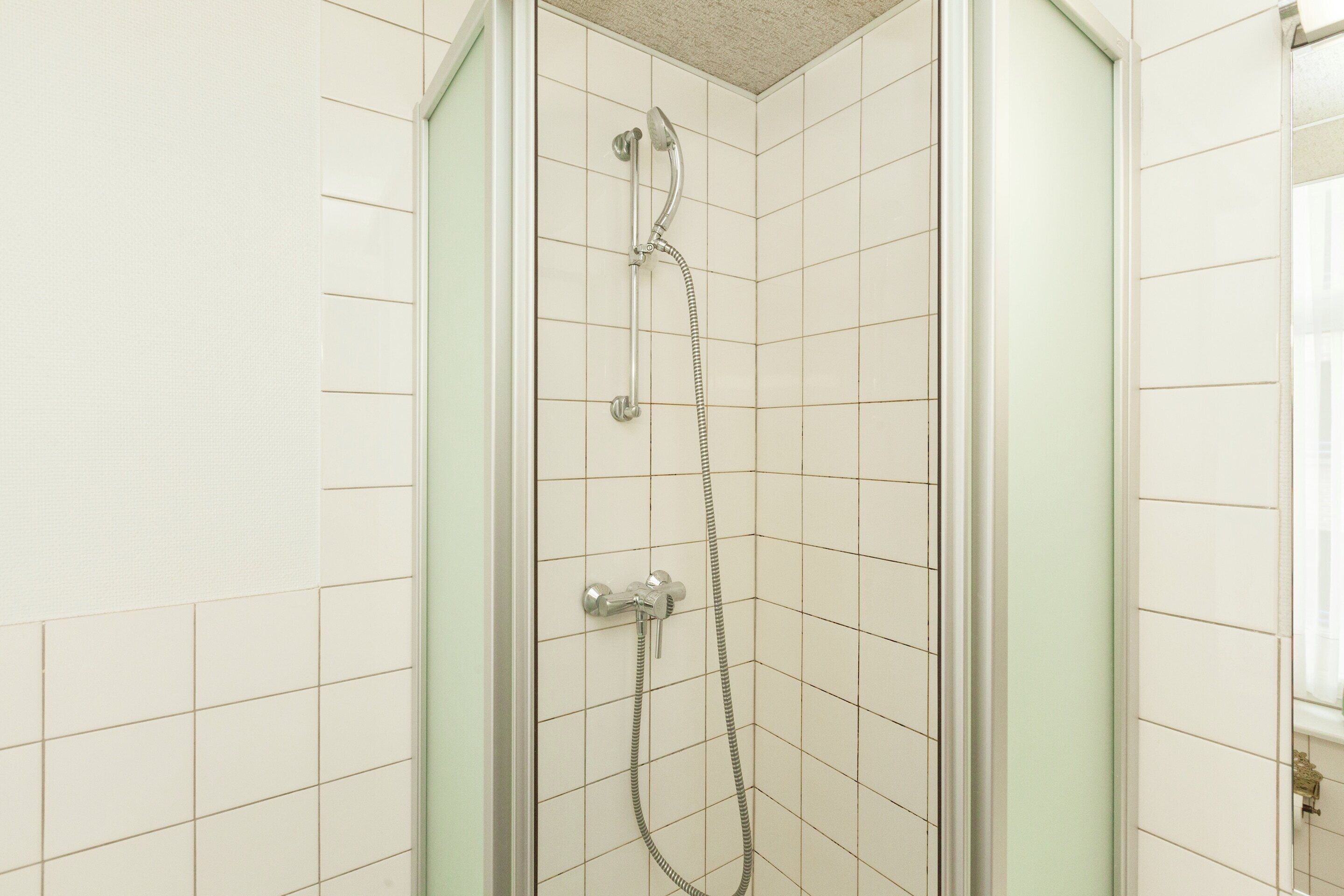 A shower with a handheld showerhead and a wall-mounted faucet.