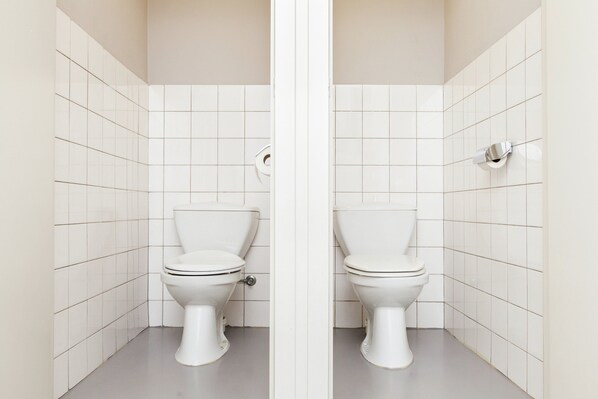 Un baño con dos inodoros, paredes de azulejos blancos y suelo gris.