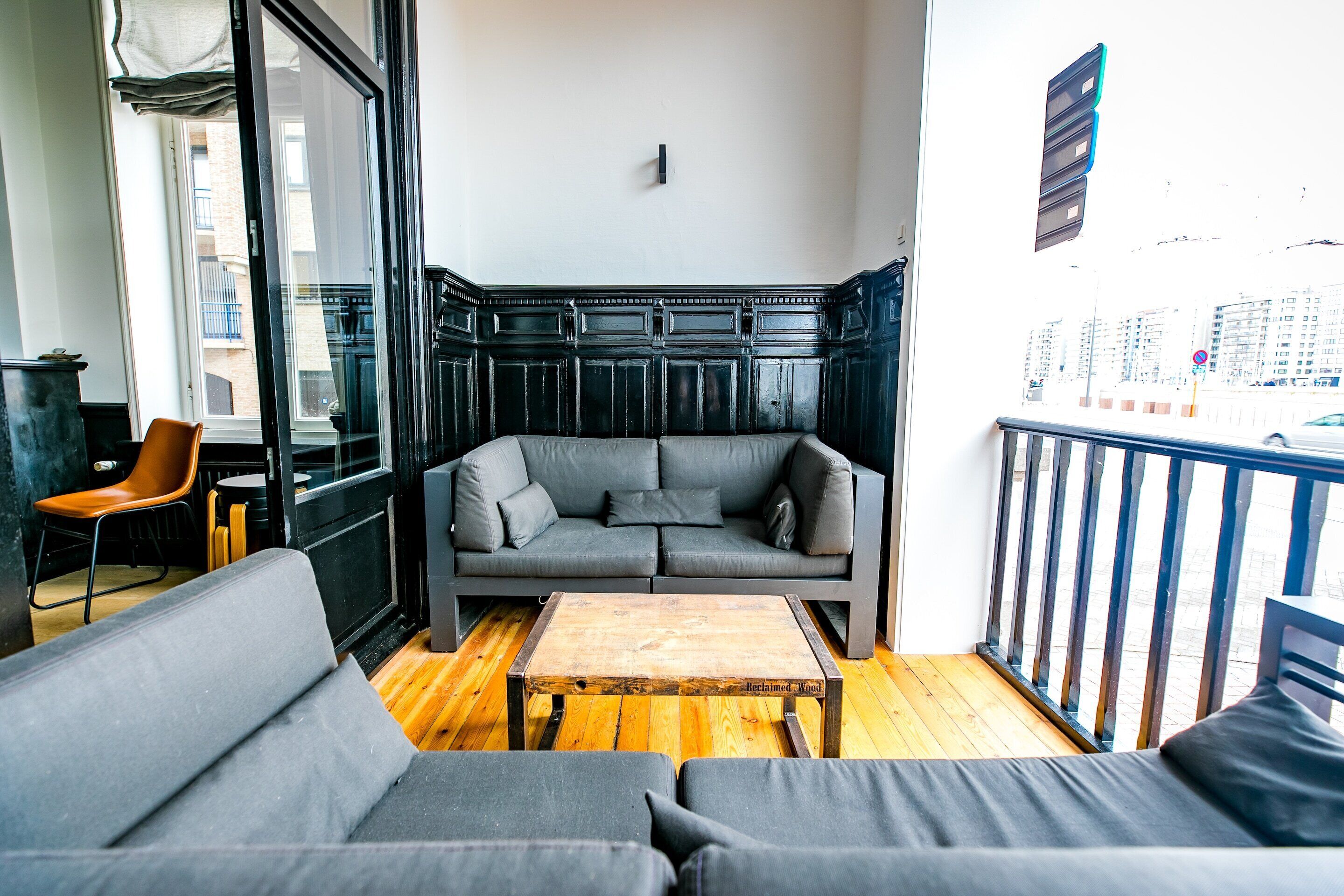 A modern living room with a grey sofa, a wooden coffee table, and a view of the city through large windows.