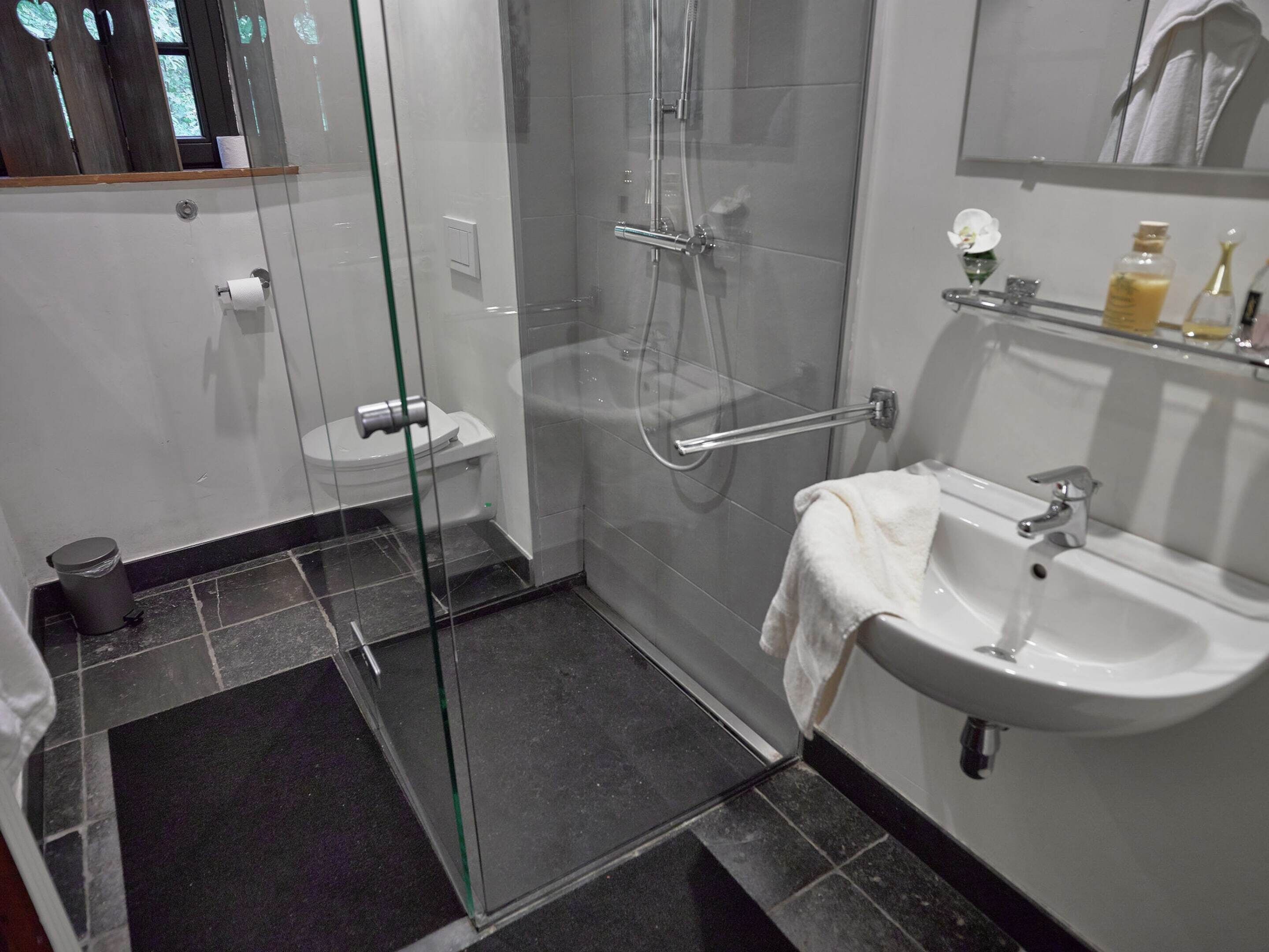 Un baño moderno con cabina de ducha de vidrio, un lavabo blanco y un inodoro.