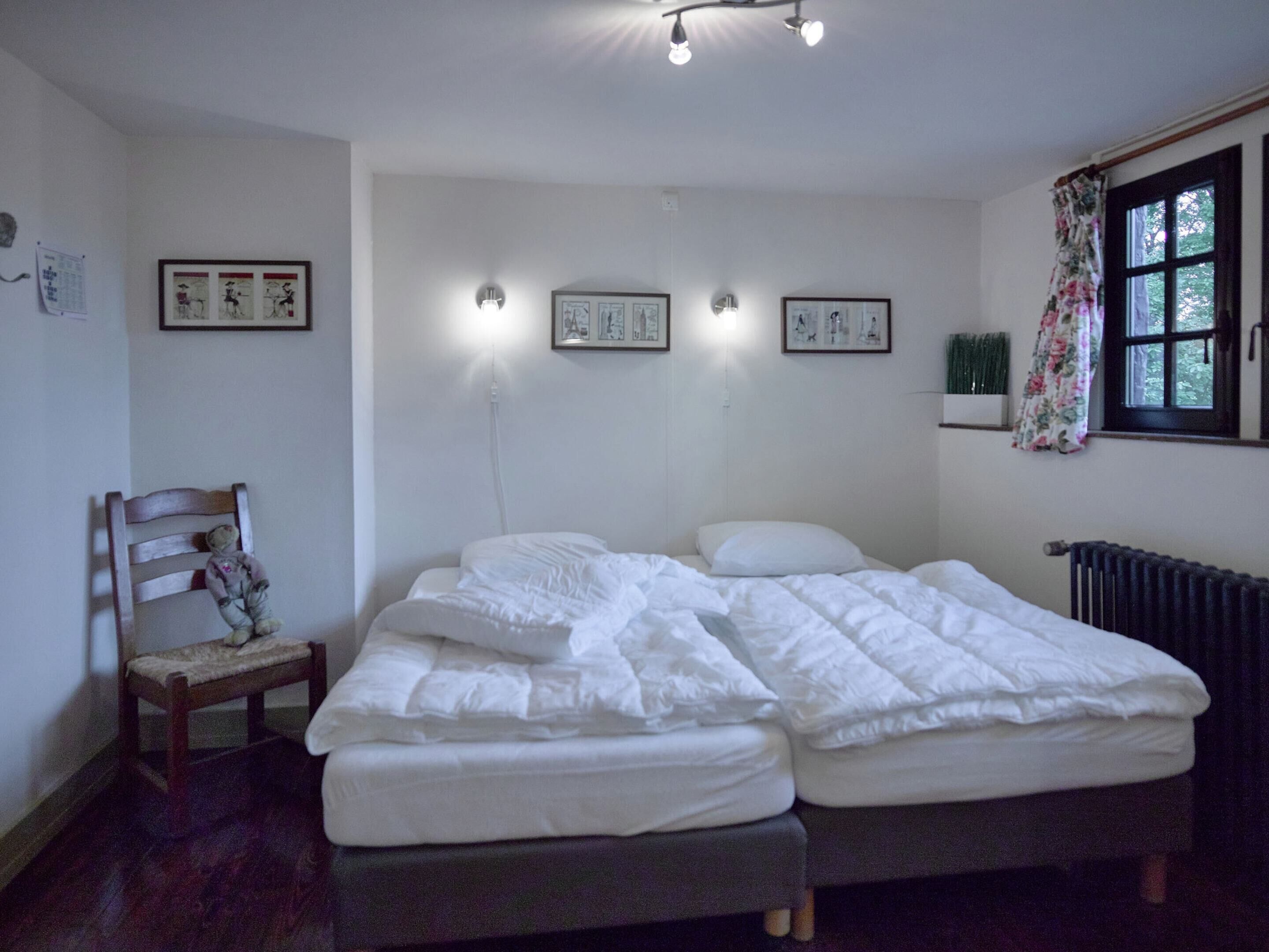 Un dormitorio con dos camas, una silla y luces fijadas a la pared.