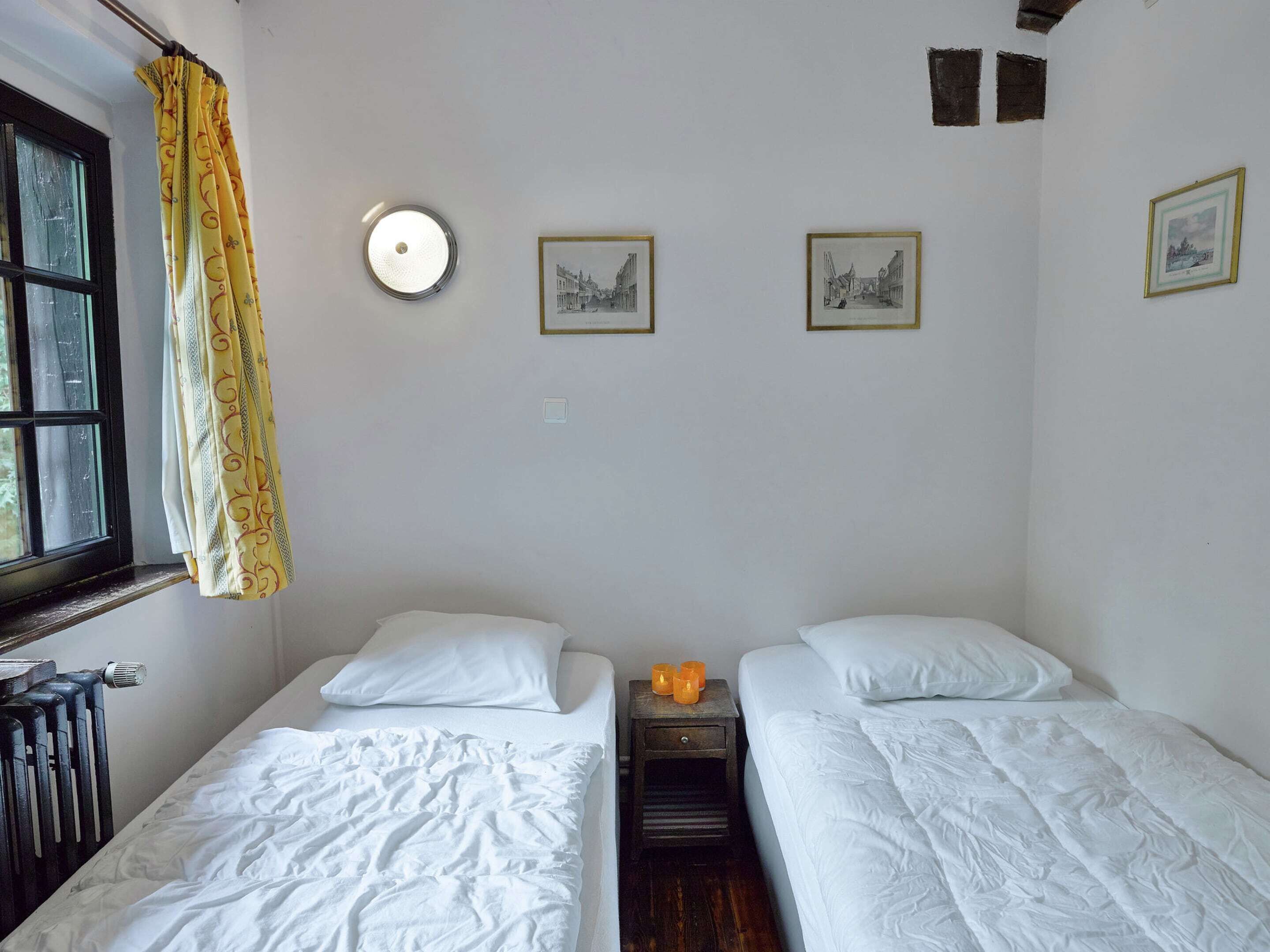 A room with two beds, a window with curtains, and three framed pictures on the wall.