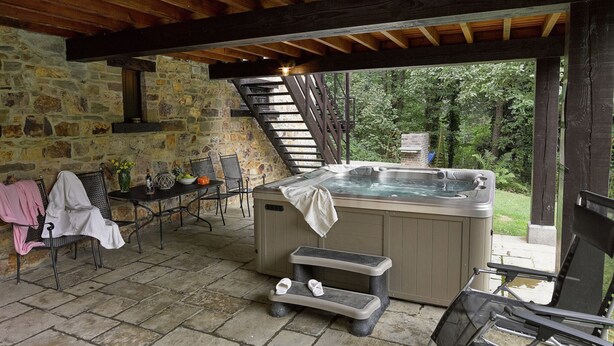 A stone-walled room with a hot tub, a table with chairs, and a staircase leading to an upper level. - Spacious Villa in Liege (Spa)